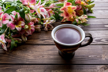 cup of tea and Alstroemeria on the wooden background. flowers on a brown background. copy text. beautiful bouquet.