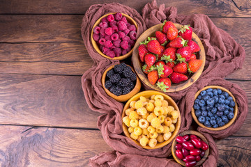 Blackberry, strawberry, yellow and red raspberries, dogwood in wooden bowls on a dark wooden old background in vintage style.