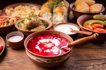 Traditional Ukrainian dishes in clay pots - borsch with sour cream, baked potatoes, garlic pampushki, sauerkraut, lard, canned tomatoes and cucumbers, mushrooms