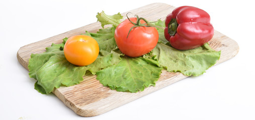  Culinary composition of fresh natural vegetables on a white background: red, yellow tomatoes, bell peppers and green fresh salad lie on a wooden cutting board