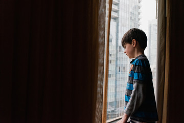 Boy looking at city through window