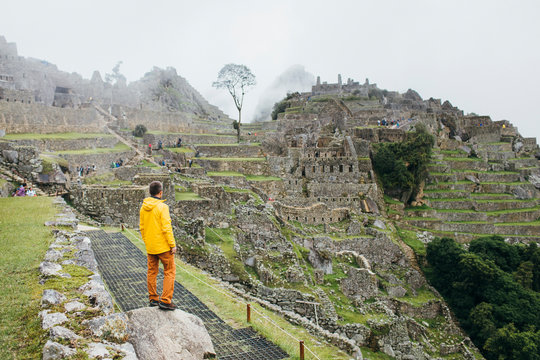 A man in a yellow jacket is standing near ruins of Machu Picchu, Peru