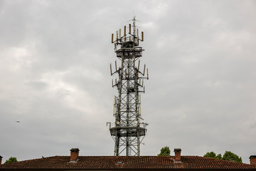 Antenna used for mobile phones network. Cellular radio tower behind a house roof.