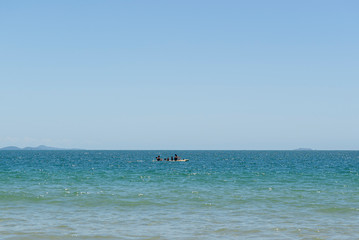 View of beautiful beach in Florianópolis, Brazil. Two men kayaking in the turquoise sea under beautiful clear sky on vacation day in tropical summer. Concept of outdoor activity in contact with nature