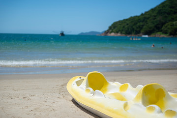 Faded yellow two-seater kayak moored on the sand of a beautiful beach in Brazil in a sea and blue...