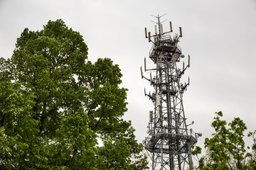 Antenna used for mobile phones network. Cellular radio tower and trees against grey sky.