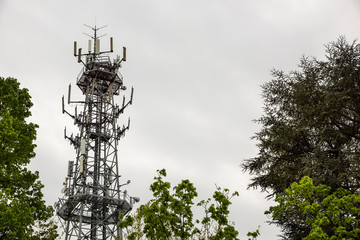 Antenna used for mobile phones network. Cellular radio tower and trees on a cloudy day.