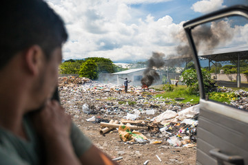 View from vehicle of worker at dump burning garbage.