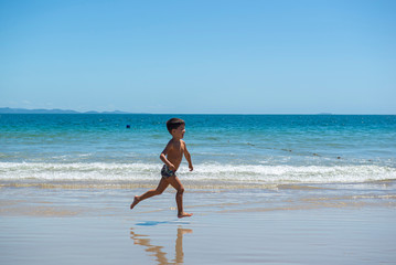 Fototapeta na wymiar Little boy running on beach beside blue sea in a sunny day of summer.