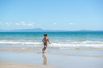 Little boy running on beach beside blue sea in a sunny day of summer.
