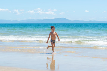 Little boy running on beach beside blue sea in a sunny day of summer.
