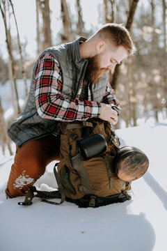 man with bead wearing flannel and vest kneels in snow with pack