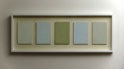 Frame hanging on wall with five empty spaces in green and blue colours