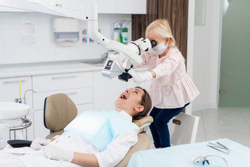 A dental doctor with her little female patient. Little girl looking into a woman's mouth through a dental microscope. Child playing a doctor concept