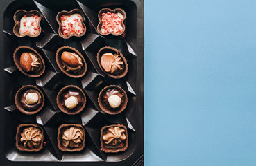 Box of beautiful chocolate candy with nuts on a blue background, top view with copy space.