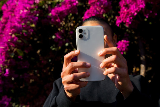 woman using cell phone outdoors in front of flower blossoms