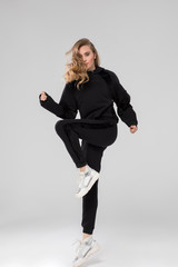 cute blonde girl posing in chic long sleeve black sports wear. white sneakers. white background.
