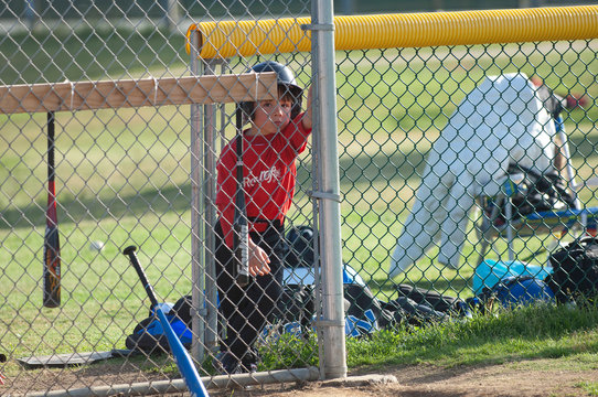 Player standing behind chain link fence in dugout ready to go to bat