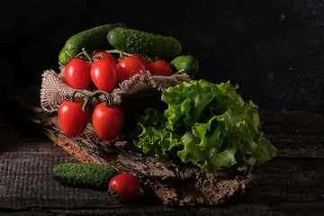 Vegetables, ripe juicy red tomatoes, young cucumbers and lettuce on the table. Ingredients for vegetable salad. Dark food photo.