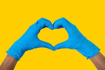 Human wearing blue gloves rising hands making finger heart shape, disposable rubber glove for professional medical safety and hygiene protection from Coronavirus disease COVID-19 Yellow background
