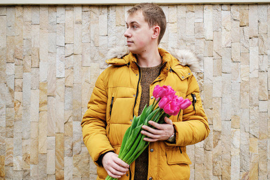 blond man in a yellow winter jacket with a bouquet of tulips in hands