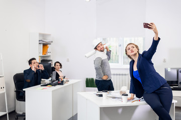 Employees having fun in the office, posing and taking selfies with a smartphone