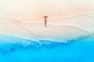 Aerial view of the beautiful young woman lying on the white sandy beach near sea with waves at sunset. Summer travel. Top view of slim girl, transparent blue water. Indian Ocean in Zanzibar, Africa - obrazy, fototapety, plakaty