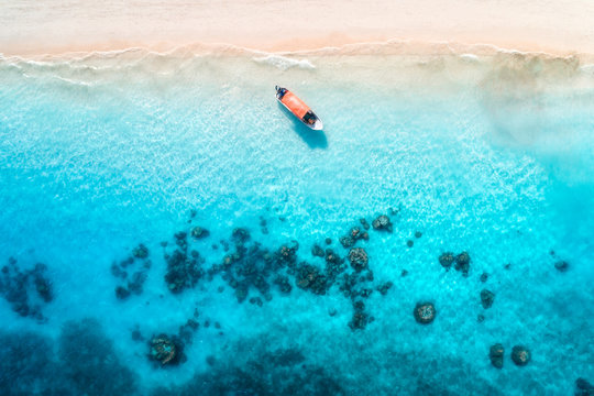Aerial view of alone fishing boat in transparent blue water at sunset in summer. Top view of boat from drone , sandy beach in Zanzibar. Travel. Tropical seascape with motorboat, sea. View from above © den-belitsky