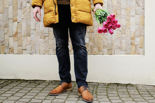 blond man in a yellow winter jacket with a bouquet of tulips in hands