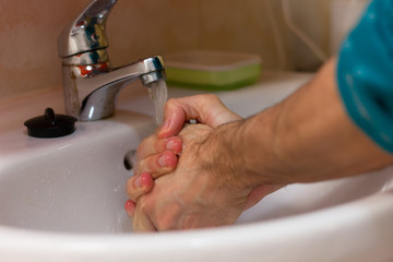 Hands of man washing with water on white sink. Rubber drain stopper by silver faucet. Cleaning, skin care, hygiene concepts