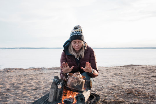 woman warming her hands on a camp fire waiting for water to boil