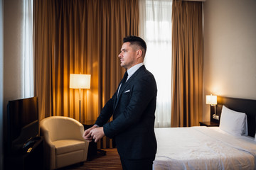 Young handsome businessman adjusting his jacket, dressing up at his luxury hotel suite preparing for a meeting during his business trip. A stylish, elegant, masculine, confident, focused executive