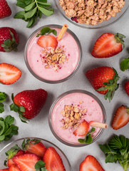 Strawberry smoothie with coconut milk with granola and nuts in a glass with a bamboo straw on a light gray background top view