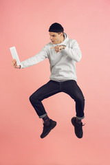 Fototapeta na wymiar Using tablet. Caucasian young man's modern portrait isolated on pink studio background. Beautiful male model in high jump. Concept of human emotions, facial expression, sales, ad. Copyspace.