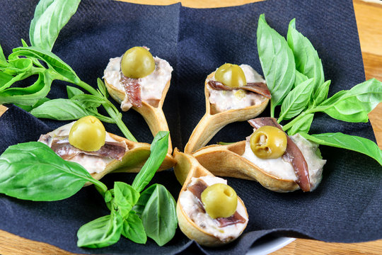 Tarlets with anchovies, olives, sauce and green herbs for eating. Healthy seafood fast snack.