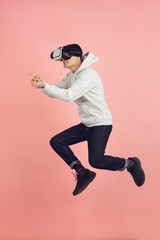 Playing with VR-headset. Caucasian young man's modern portrait isolated on pink studio background. Beautiful male model in high jump. Concept of human emotions, facial expression, sales, ad. Copyspace
