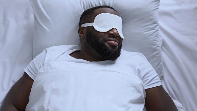 Exhausted man in sleep mask trying to fall asleep after long flight, jet lag
