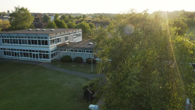 Aerial drone view taking off in front of a generic school building during a summer sunset