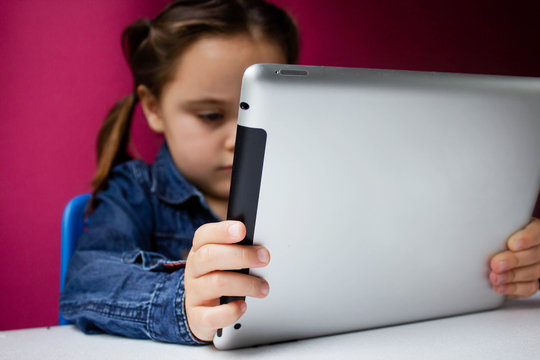 A smiling little girl watching an online video lesson on a smartphone at home, a Cute happy little child calling on a mobile phone with a teacher or tutor, home learning concept