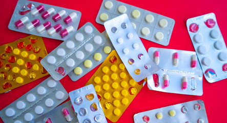 Close up of medical blister packs with tablets on red background. Packs with various tablets. Concept of threat of various diseases.