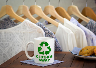 Clothes swap icon and text on mug in front of clothes at swap party stall, sustainable fashion and...