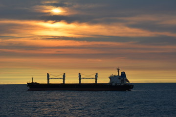 Obraz premium A cargo ship silhouetted against a setting sun sky.