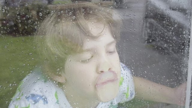 Boy looking out of window on a rainy day themes of sadness solitude emotions