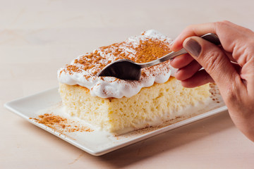 Woman's hand picking up a delicious piece of three milk cake, Latin American dessert