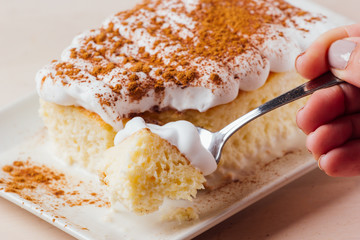 Woman's hand picking up a delicious piece of three milk cake, Latin American dessert