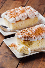 Two pieces of a delicious three milk cake dessert on a wooden background