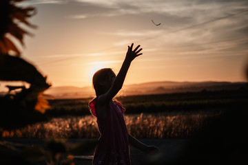 Silueta de niña lanzando hoja al aire al atardecer