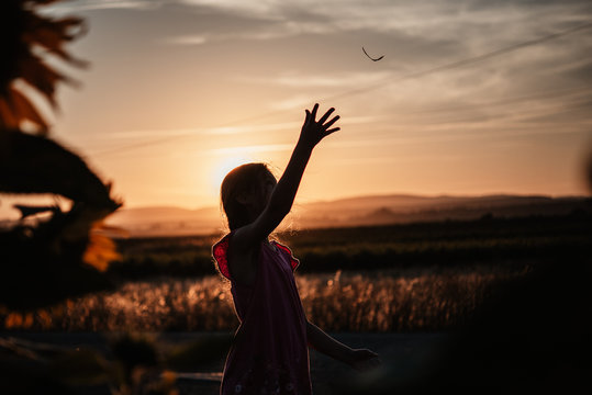 Silueta de ni&ntilde;a lanzando hoja al aire al atardecer