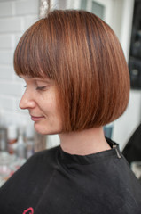 Haircut bob on bright mahogany hair of a young woman in a beauty salon