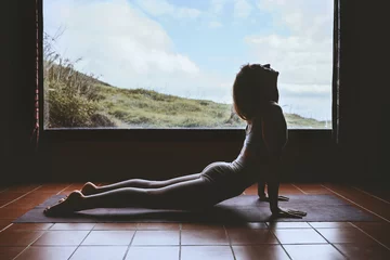 Fotobehang Silhouette of young woman practicing yoga indoors © nataliaderiabina